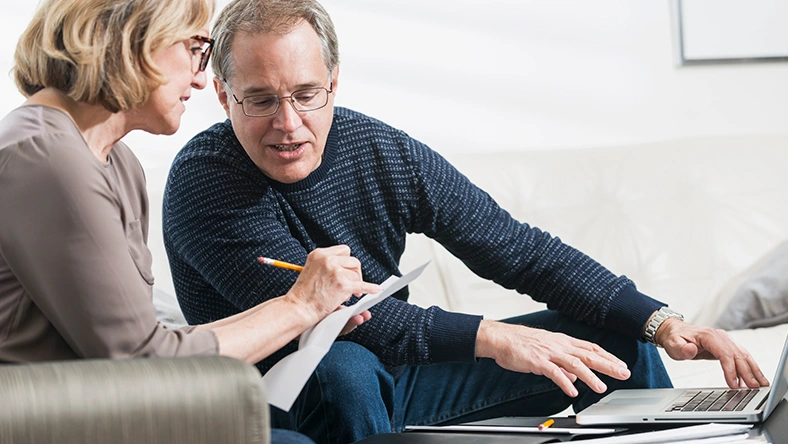 Two adults reviewing financial documents and using a laptop, representing retirement planning and catch-up savings strategies.
