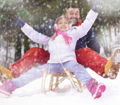 Father and daughter having fun in the snow on a sled.